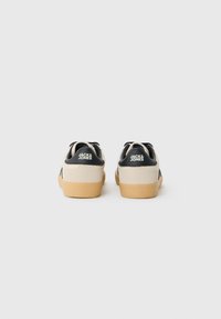 Canvas sneakers, beige with black accents, featuring a rubber sole and heel tags. Stitching details visible. Designed for casual wear.