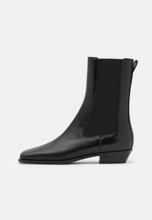 Bottine noire en cuir avec panneau latéral élastique, talon bas incliné, bout rond et languette arrière sur fond uni.