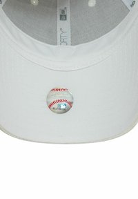 Weißer Baseball-Cap mit flachem Schirm, strukturiertem Stoff und einem glänzenden Anstecker auf der Vorderseite, der ein Baseball-Design mit roter Naht zeigt.