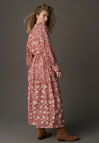 Rochie lungă roșie cu motive florale albe, mâneci lungi și talie strânsă. Purtați cu cizme până la gleznă maro. Textură netedă.
