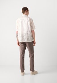 Cămașă cu mânecă scurtă, de culoare deschisă, cu un model subtil de frunze, asortată cu pantaloni maro și adidași bej. Material neted, croială lejeră.