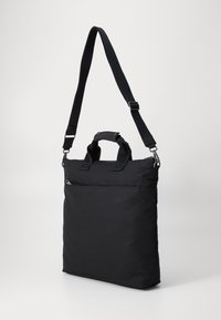 Sac à main noir en tissu texturé ; doté d'une poignée supérieure, d'une bandoulière ajustable et d'une poche zippée à l'avant. Design épuré et minimaliste.