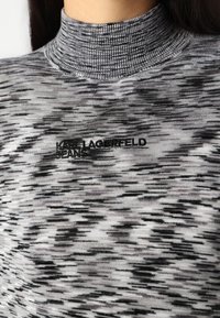 Juodai baltas golfas su tekstūrine, abstrakčia rašalo. Siuvinėtas logotipas "KARL LAGERFELD JEANS" priekyje.