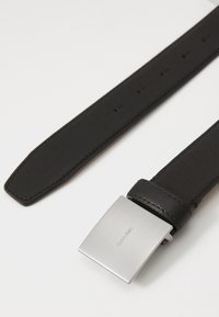 Ceinture en cuir noir avec une finition lisse, dotée d'une boucle rectangulaire en métal argenté gravée "Calvin Klein." Quatre trous de réglage visibles.