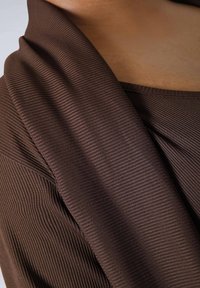 Brown ribbed fabric drapes softly around the neckline, with a smooth texture and a wide, flowing shape that transitions into a fitted design.