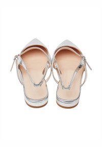 Ballerines argentées à bout pointu avec des brides de cheville et des talons bas sur un fond blanc.