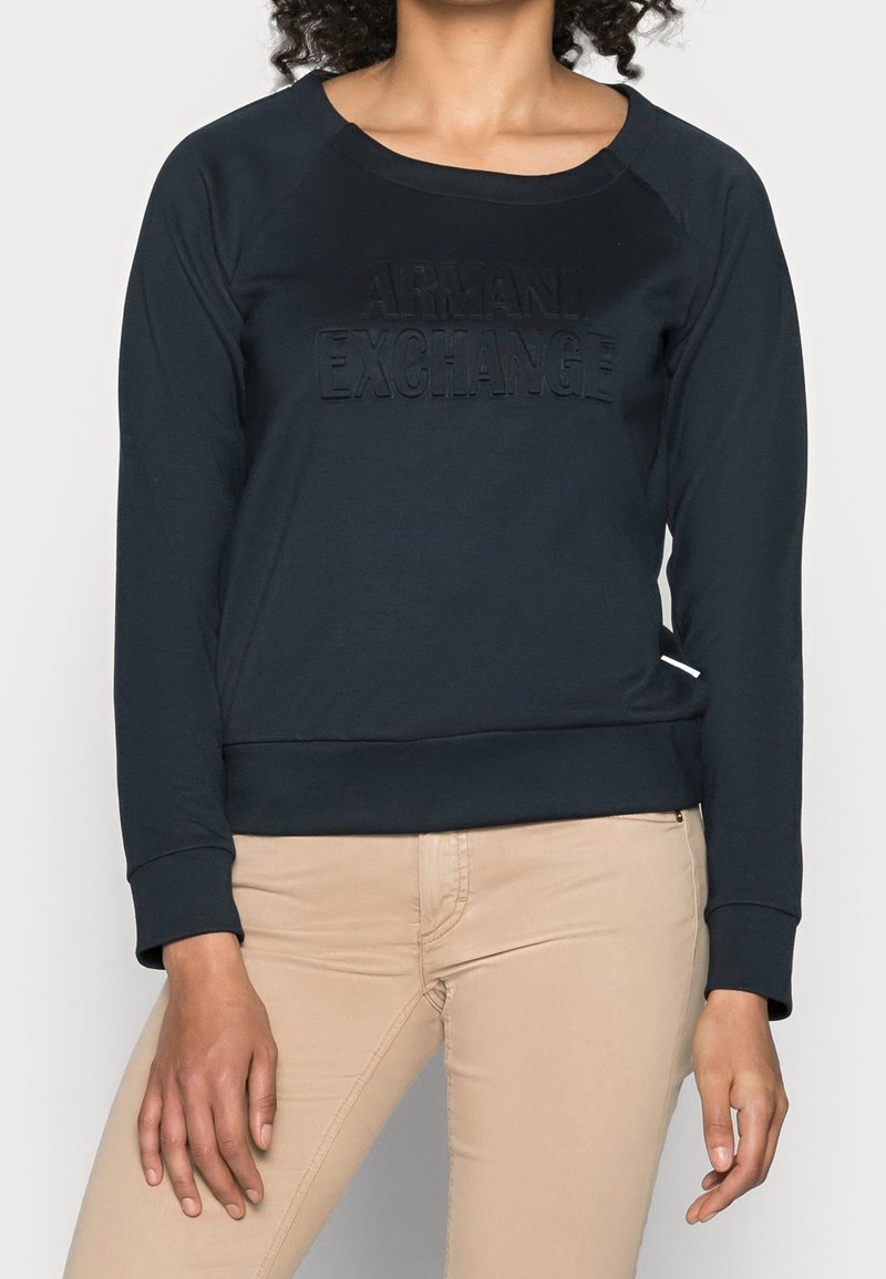 Černá mikina s kulatým výstřihem, raglánovými rukávy a vyraženým logem "ARMANI EXCHANGE" na přední straně. Měkká tkanina a vypasovaný pas.