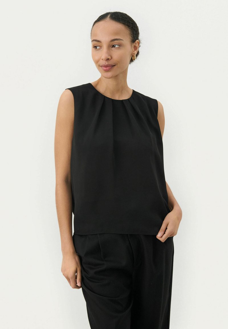 Top nero senza maniche con scollatura plissettata, realizzato in tessuto liscio. Abbinato a pantaloni neri a gamba larga, con un fit rilassato.
