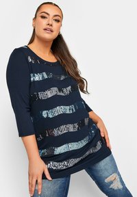 Maglia a maniche lunghe navy con strisce orizzontali di paillettes in argento e blu. Tessuto morbido con scollo rotondo e vestibilità comoda.