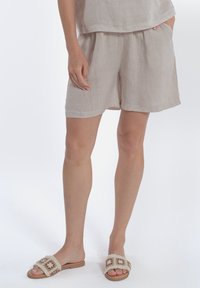 Pantaloni corte in lino di un beige chiaro con una vita elastica e tasche laterali, abbinati a sandali decorativi con una fascetta con motivo.