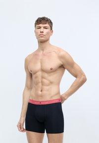 Mustat boxershortsit, joissa on punainen TOMMY HILFIGER -brändätty vyötärö, valmistettu joustavasta materiaalista, lähellä vartaloa istuva malli ja sileä pinta.