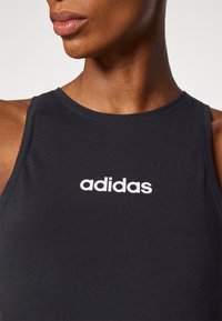 Svart träningslinne i stretchigt material, med rund halsringning och vitt "adidas"-logotyp på framsidan.