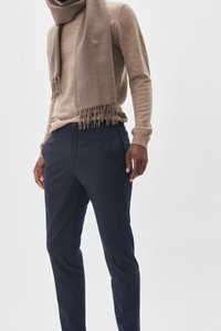 Pull en tricot beige avec un col rond et des manches longues, associé à un pantalon noir marine ajusté et une écharpe à franges marron clair.
