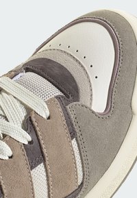 Tenisice sa kombinacijom bež i smeđeg antilopa uz mrežasti panel. Opremljene su detaljima od teksturirane kože i kremastim vezicama na gumenom potplatu.