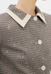 Koszula z kołnierzykiem z materiału w kratkę z beżowymi akcentami. Posiada delikatny blask dzięki cekinom, prezentując dopasowany krój oraz kontrastujące faktury.