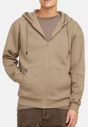 Hooded zip-up sweatshirt in taupe, featuring a kangaroo pocket, drawstrings, and ribbed cuffs. Layered over a brown T-shirt.