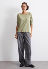 Lys grønn langermet skjorte med scoop-hals, kombinert med vide grå jeans og svarte chunkysko. Enkelt, avslappet design.