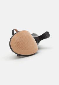 Black shoe with a rounded sole, featuring a tan rubber bottom with horizontal grooves for grip and a smooth black leather upper.