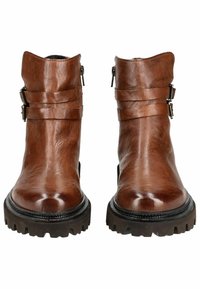 Botas de cuero marrón hasta el tobillo con un acabado suave, cremalleras laterales y dos correas estrechas en la parte superior. Suelas de goma gruesas y resistentes.