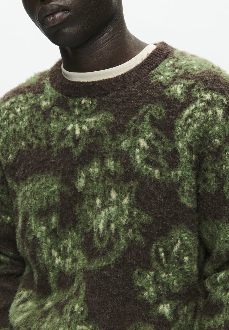 Pull en laine brun et vert à motifs, avec un tricot texturé, doté d'un col rond et d'une finition douce et duveteuse. Motifs de feuilles remarquables.