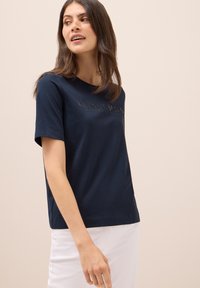 Camiseta de algodón azul marino con cuello redondo, mangas cortas y texto en relieve "CIELOS ETERNOS" en el frente.