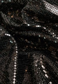 Schwarzer Paillettenstoff mit kleinen, reflektierenden Quadraten, der eine strukturierte, schimmernde Oberfläche erzeugt. Das Material ist leicht und fällt gut.