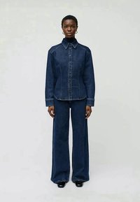 Dark denim jacket with a pointed collar, front buttons, and matching wide-leg jeans. Both pieces feature subtle stitching and a structured design.