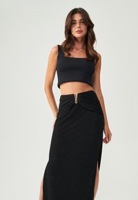 Melna cropped top ar kvadrātveida dekoltē, apvienots ar melnu garu svārku ar priekšējo šķēlumu un savilkšanas detaļu, ko akcentē metāla rāvējslēdzis.