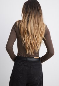 Pikkade varrukatega pruun topp, mis on kombineeritud kõrge vöökohaga mustade denimitekingadega. Juuksed on pikad, lainelised ja ombre, üleminek tumedatest helgetesse toonidesse.