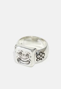 Silver ring med ett upphöjt, leende ansiktsdesign med texturerade prickar. Ytterligare blommor accent på sidan. Slät yta, rundade kanter.