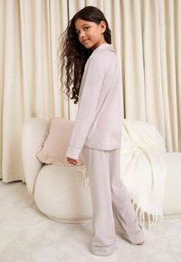 Conjunto de pijama de color rosa claro hecho de una tela suave. Cuenta con mangas largas, puños y pantalones de corte relajado. Textura suave y ligero brillo.