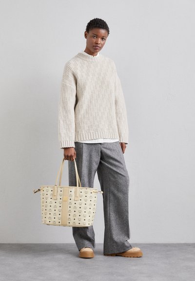 Pull beige texturé avec un col montant, pantalon gris à jambes larges et un sac à main crème avec un accent à motifs et des poignées doubles.
