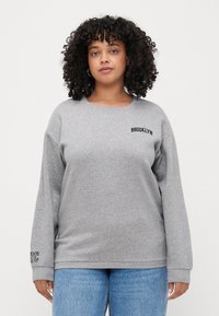 Gray sweatshirt with a round neckline and dropped shoulders. Features "BROOKLYN" text on the chest and "NYC" on the sleeve. Soft fabric.