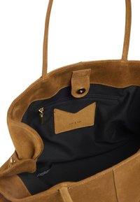 Sac fourre-tout en daim couleur fauve avec une texture douce. L'intérieur comprend une doublure noire, une poche zippée et une étiquette de marque. Comprend des poignées courtes.