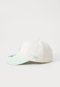 Kokvilnas beisbola cepure off-white krāsā ar piparmētru zaļu vizieri. Iezīmēta ar izšūtiem logo akcentiem un sešiem ventilācijas acu caurumiem.