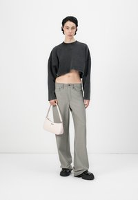 Felpa grigia a maniche lunghe, pantaloni leggeri grigio chiaro dal taglio morbido e una borsa rosa. Il modello indossa scarpe con zeppa e suola testurizzata.