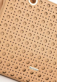 Beige leren handtas met geperforeerde ronde en driehoekige patronen, met gouden hardware en een metalen logo-accent.
