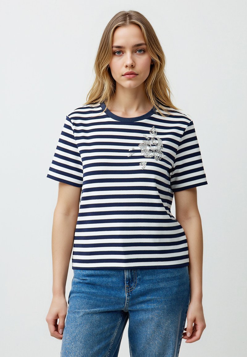 Gestreept t-shirt in marineblauw en wit met een ronde hals. Heeft een decoratieve zilveren versiering op de borst en korte mouwen.