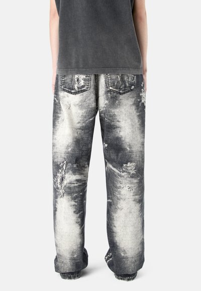 Personne portant un jean ample noir et blanc délavé à l'acide avec des détails usés et des poches arrière, associé à un débardeur gris foncé.