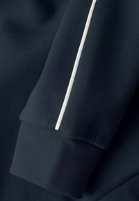Manga de sudadera azul oscuro con un puño acanalado, que presenta una delgada franja blanca a lo largo de la costura, hecha de tela texturizada.