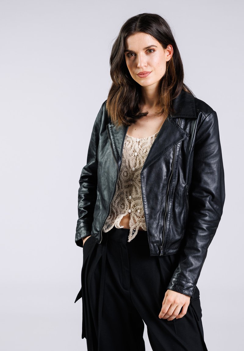 Chaqueta de motociclista de cuero negro con un diseño ajustado y grandes solapas, combinada con una blusa de ganchillo ligera y pantalones negros.