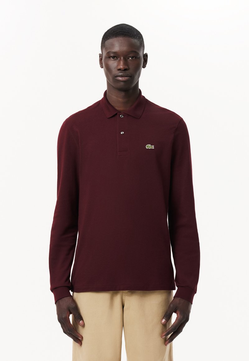 Burgundy långärmad polo med krage, med tre knappar och en grön broderad logotyp på vänstra bröstområdet.