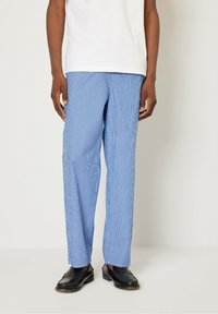Pantalones a rayas azul y blanco de tela ligera, con un corte relajado y piernas rectas, combinados con mocasines negros.