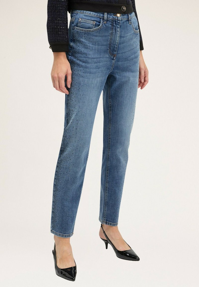Jeans de denim azul claro con corte recto, que presentan un lavado desgastado y adornos de puntos en un lado. Combinados con tacones negros brillantes.