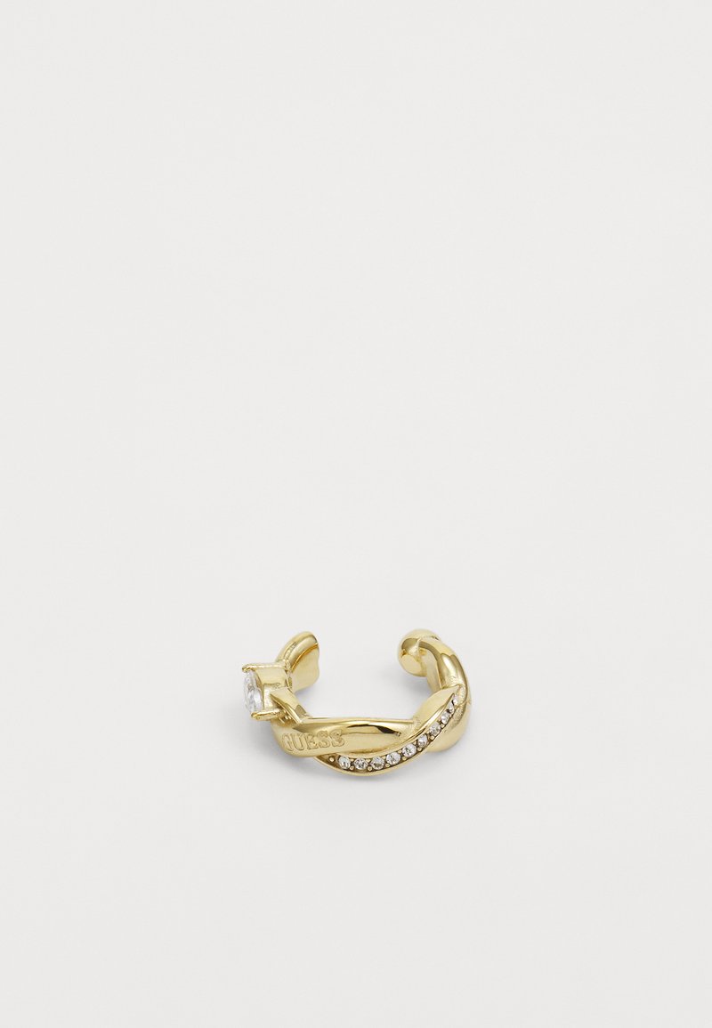 Guldring med et buet design, der har en klar sten og små hvide krystaller langs den ene side. Stemplet med mærkenavnet "Guess."