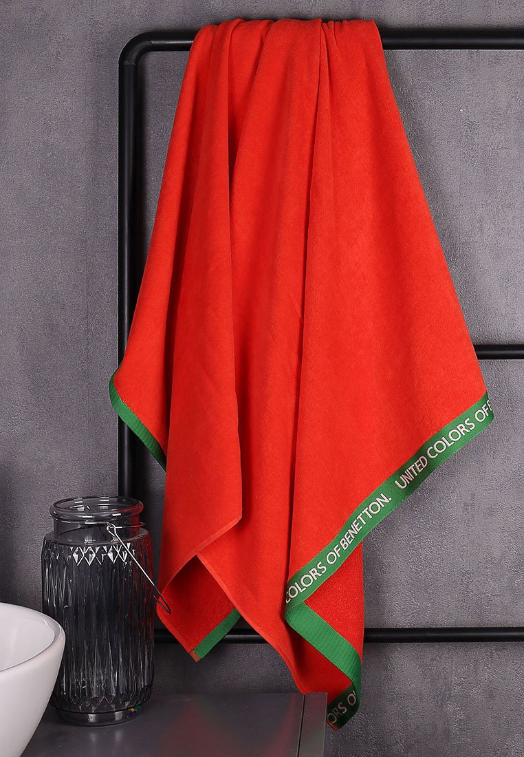 Serviette rouge avec une bordure verte, en matériau doux, comportant le texte "UNITED COLORS OF BENETTON" le long du bord.
