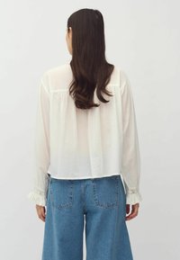 White, long-sleeve blouse with a loose fit and lace trim cuffs, paired with high-waisted blue denim jeans. Soft fabric and casual design.