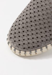 Scarpa grigia con un motivo testurizzato di forme scallopate, con perforazioni, suola crema a contrasto e cuciture decorative lungo il bordo.