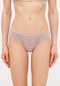 Thong met kantafwerking en een geribbeld ontwerp, in een zachte mauve kleur. Heeft een brede kanten tailleband en minimale stofbedekking.