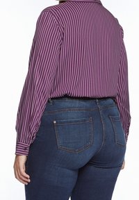 Fialová košile s dlouhým rukávem a bílými vertikálními pruhy, nošená s modrými džíny s zadními kapsami a přiléhavým střihem.